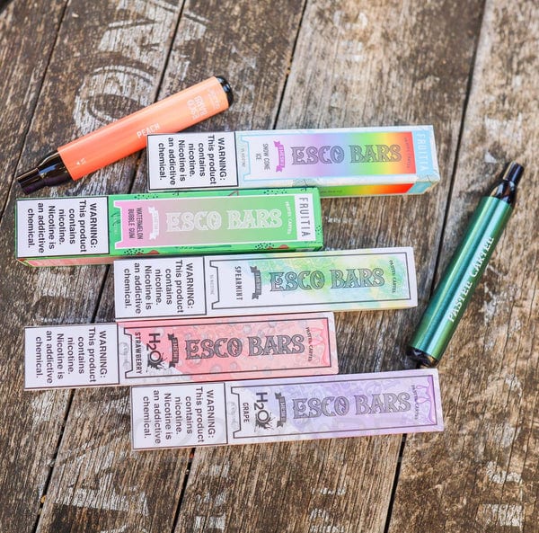 A variety of Esco Bars vapes and boxes are displayed on a wood background